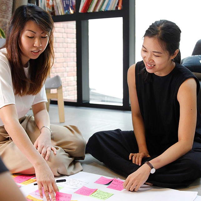 An image of two members of 55 Minutes sit on the floor, organizing colorful sticky notes for a collaborative planning session.