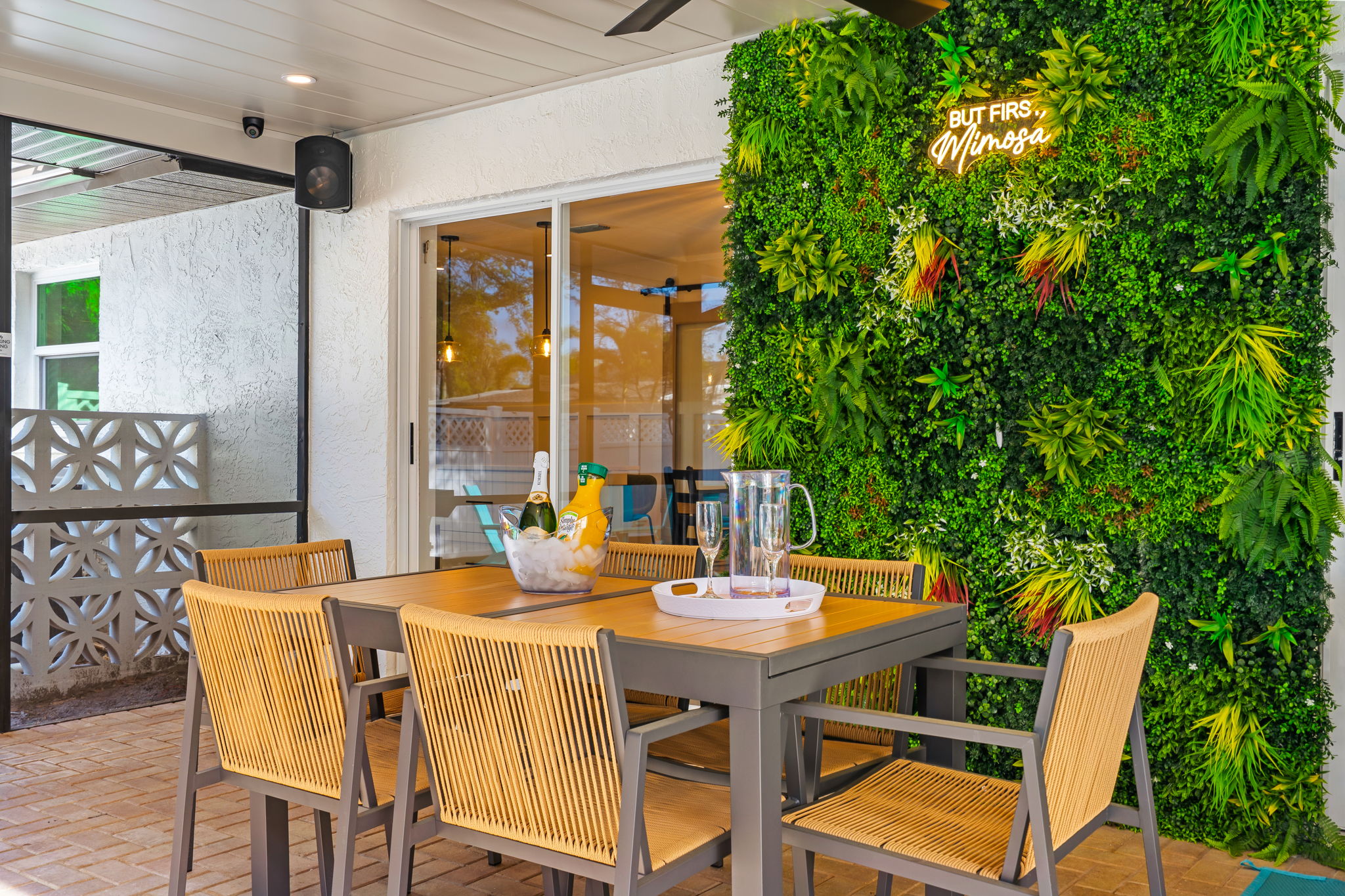 Covered patio dining table with a green plant wall, neon sign and sliding glass doors at a Sarasota Airbnb rental