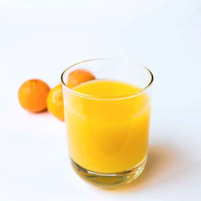 Orange juice in a glass on a white surface next to oranges
