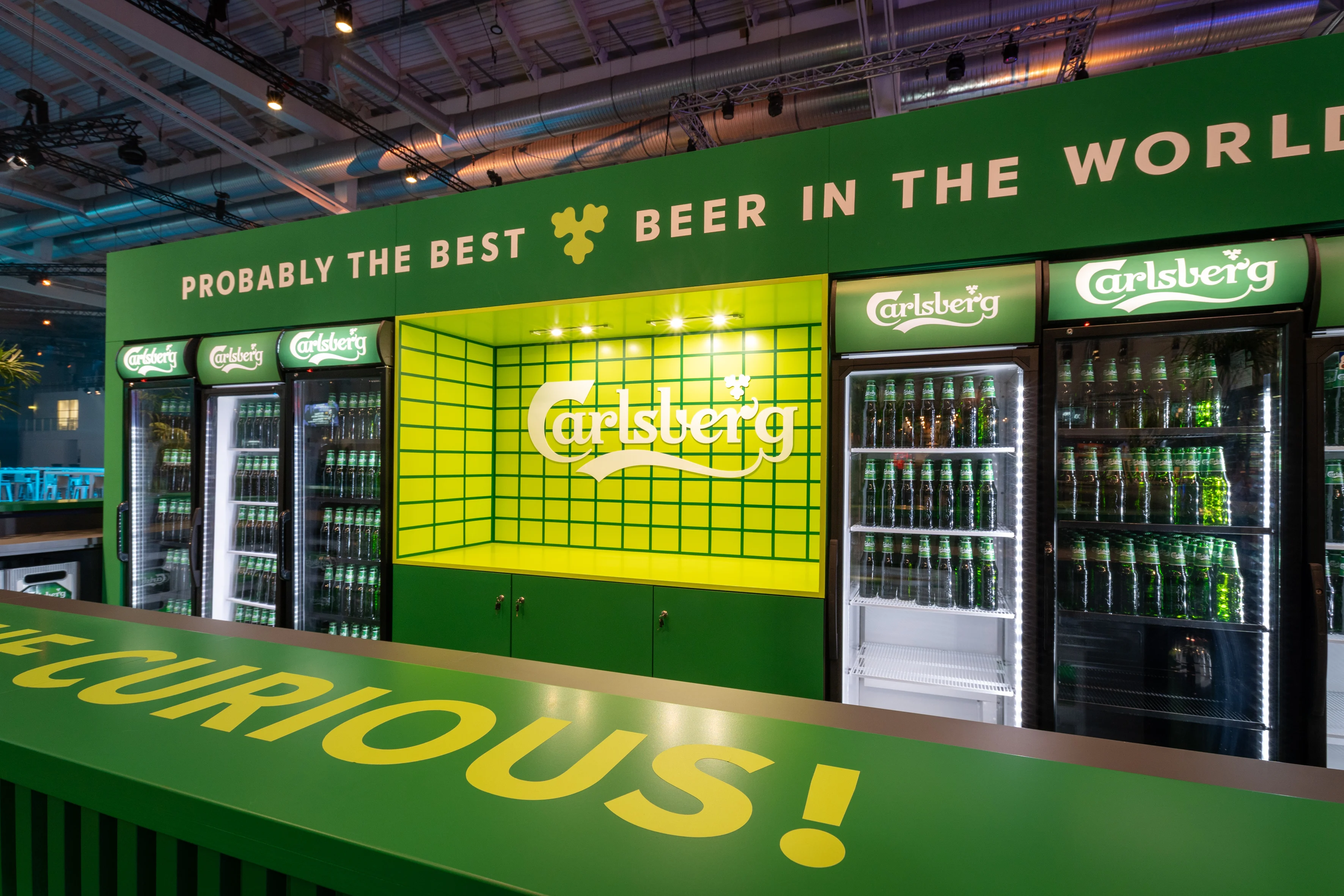 Green Carlsberg bar with beer fridges, yellow grid niche and the slogan Probably the Best Beer in the World at OMR.