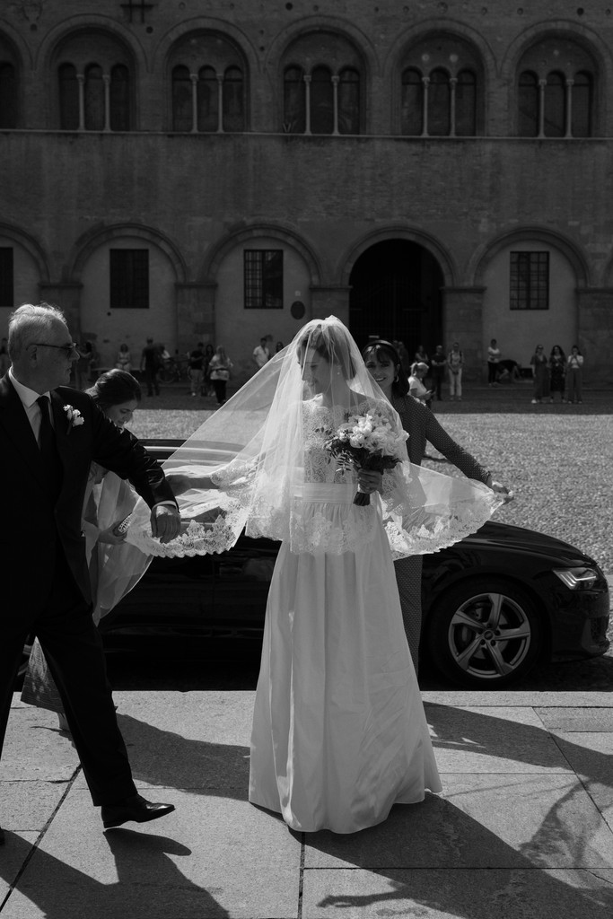 Sposa con velo lungo accompagnata dal padre in piazza davanti a villa storica, reportage di matrimonio in bianco e nero