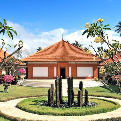 一个拥有红色瓷砖屋顶和白色墙壁的建筑，周围环绕着修剪整齐的花园和开花的树木。