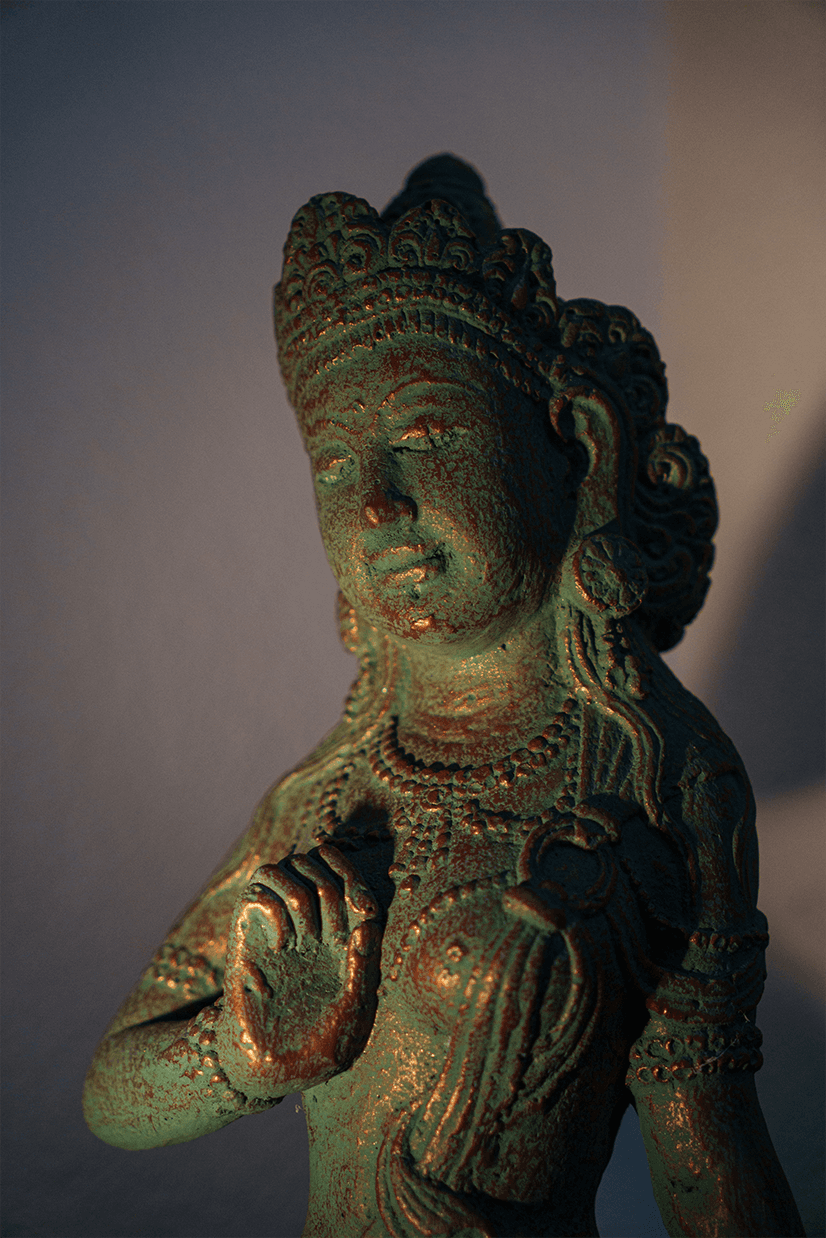 A circle of people sitting cross-legged, meditating with hands in a prayer position. Soft, warm lighting.