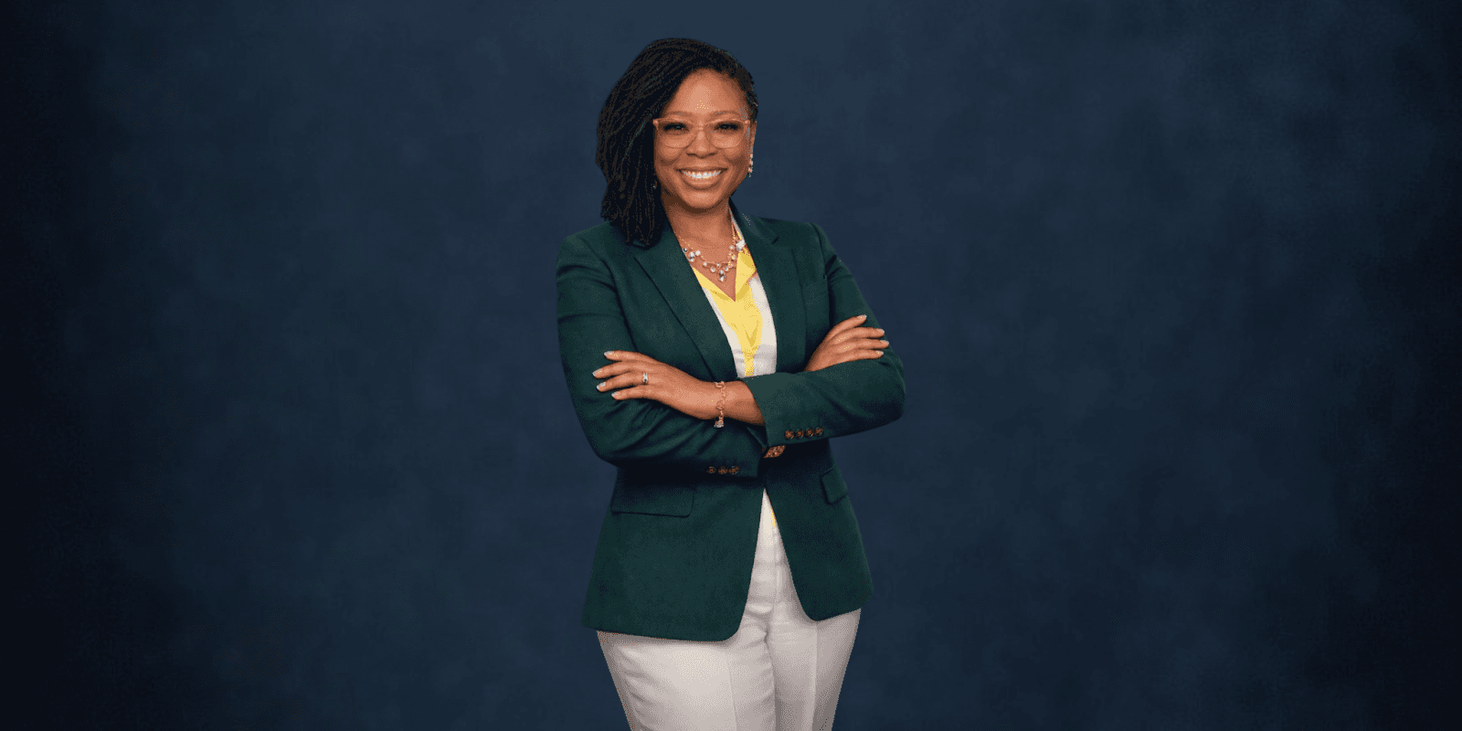 Shamicka C. Toney, an award-winning author and motivational speaker, standing confidently with arms crossed, wearing a green blazer and white pants.