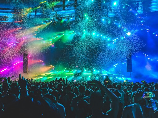 A massive crowd of people attending a concert, illuminated by vibrant lights and showered with confetti.