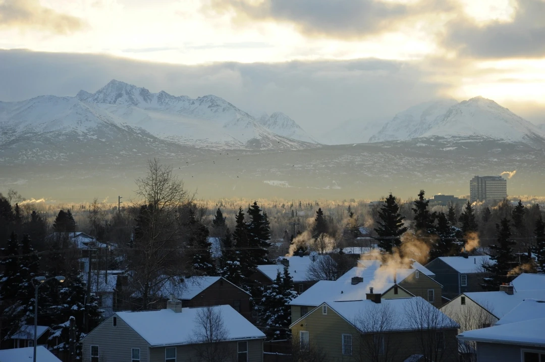 Chugach Foothills under snow, glow, saltbox houses, forest, smoke and steam rising, cloudy sky, Anchorage, Alaska, USA