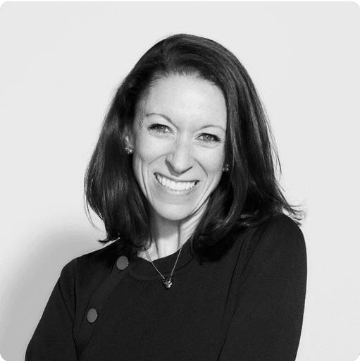 A portrait of MJ smiling woman with long, dark hair, wearing a black jacket, in a black and white image that conveys a professional and elegant aesthetic.