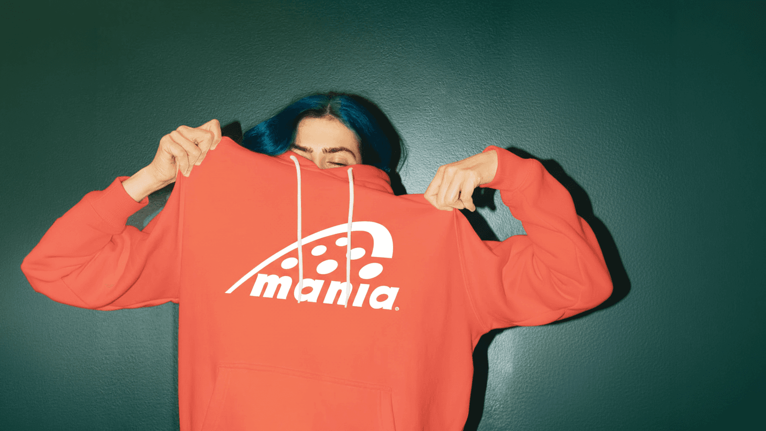 Woman with blue hair wears coral colour jumbper with logo on it. 
