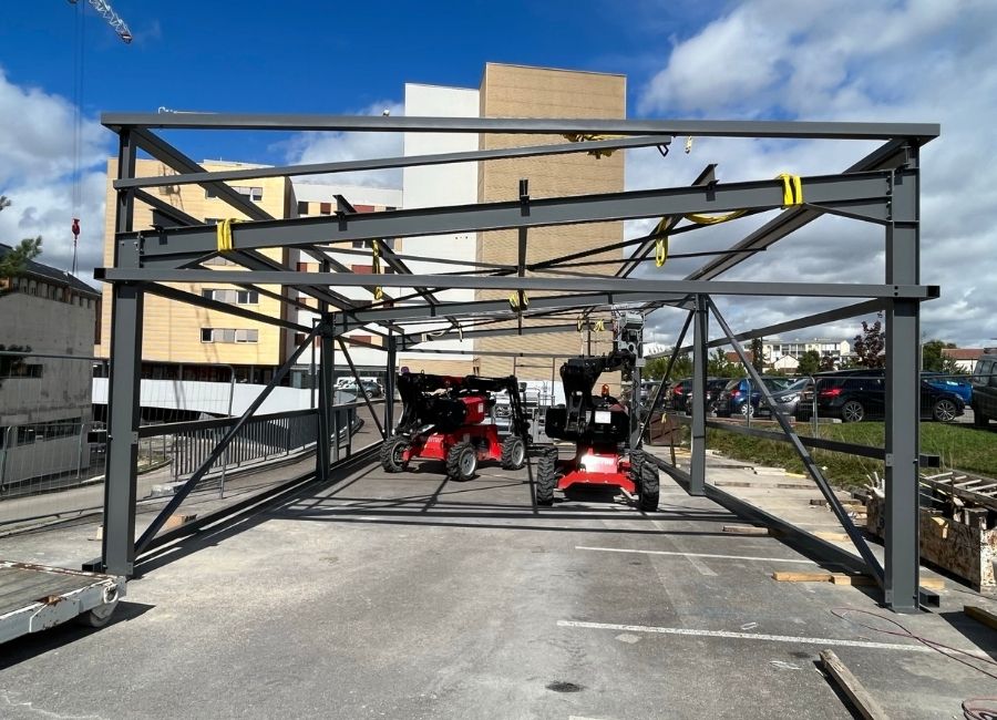 Élévation d'une charpente métallique sur chantier en ville, avec immeubles en arrière-plan.