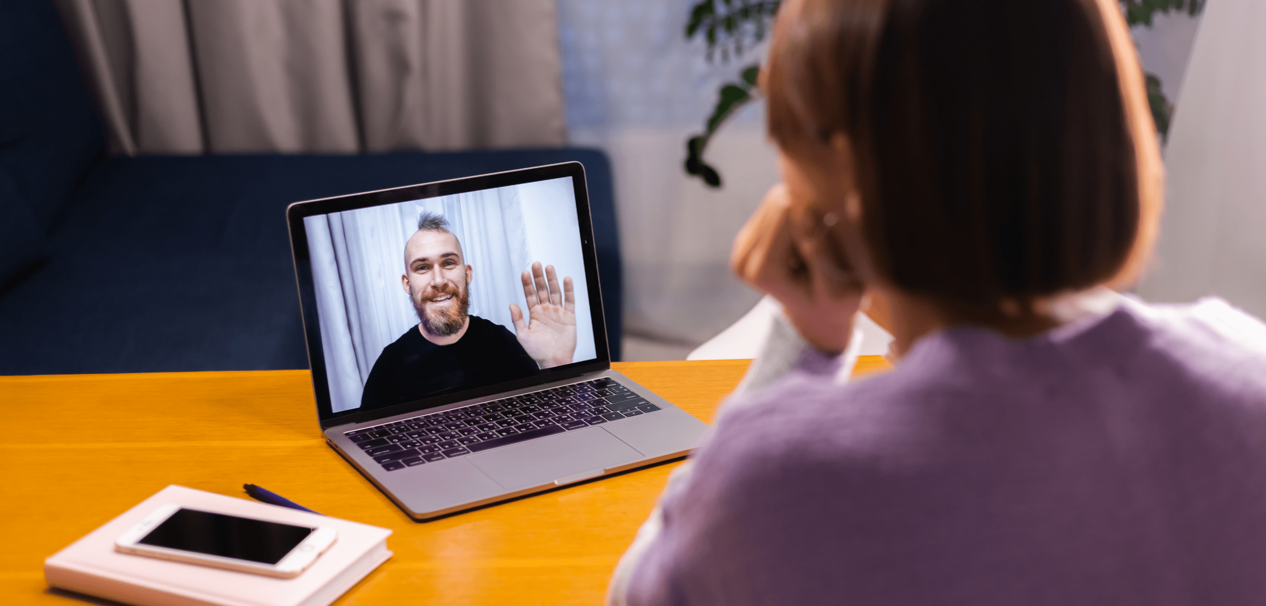 Person on a video call, smiling at a laptop screen where another person is waving during an online meeting.
