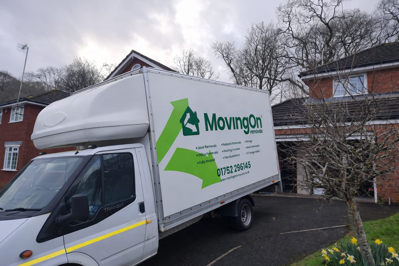 Side view of a white MovingOn Removals Luton van parked in a residential driveway, showcasing the green house logo and professional branding.