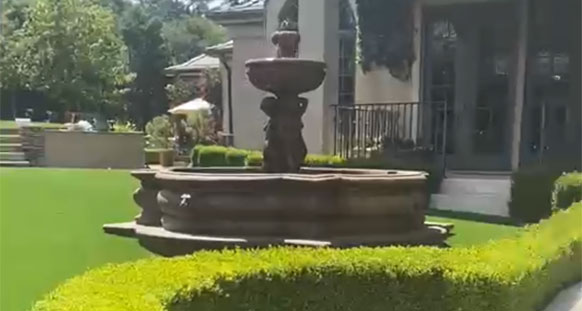Artificial turf lawn in Los Gatos surrounding a tiered stone fountain, edged by clipped boxwood hedging in front of an estate home.