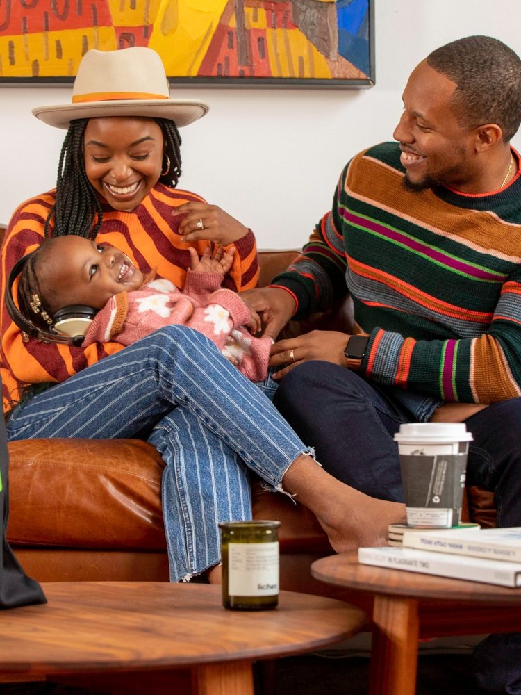 Janique & Anthony Edwards sit on a brown sofa with their child.