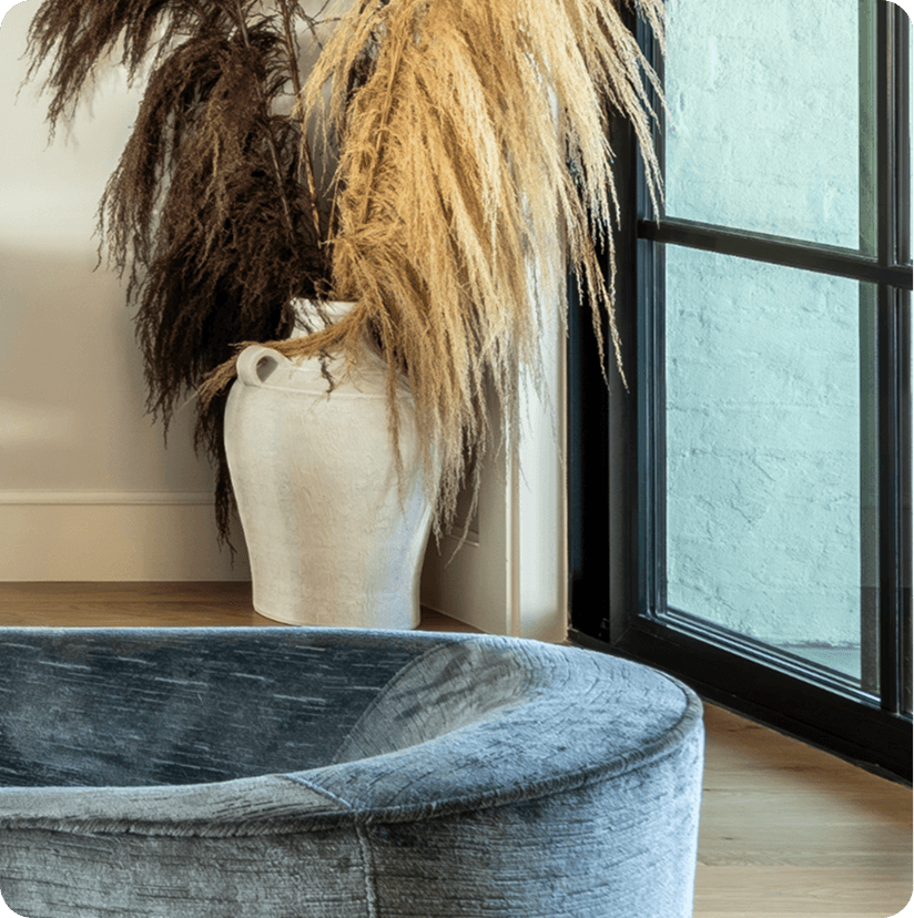 Corner of sitting room featuring dried pampas grass in ceramic vase by black-framed window with gray upholstered seating