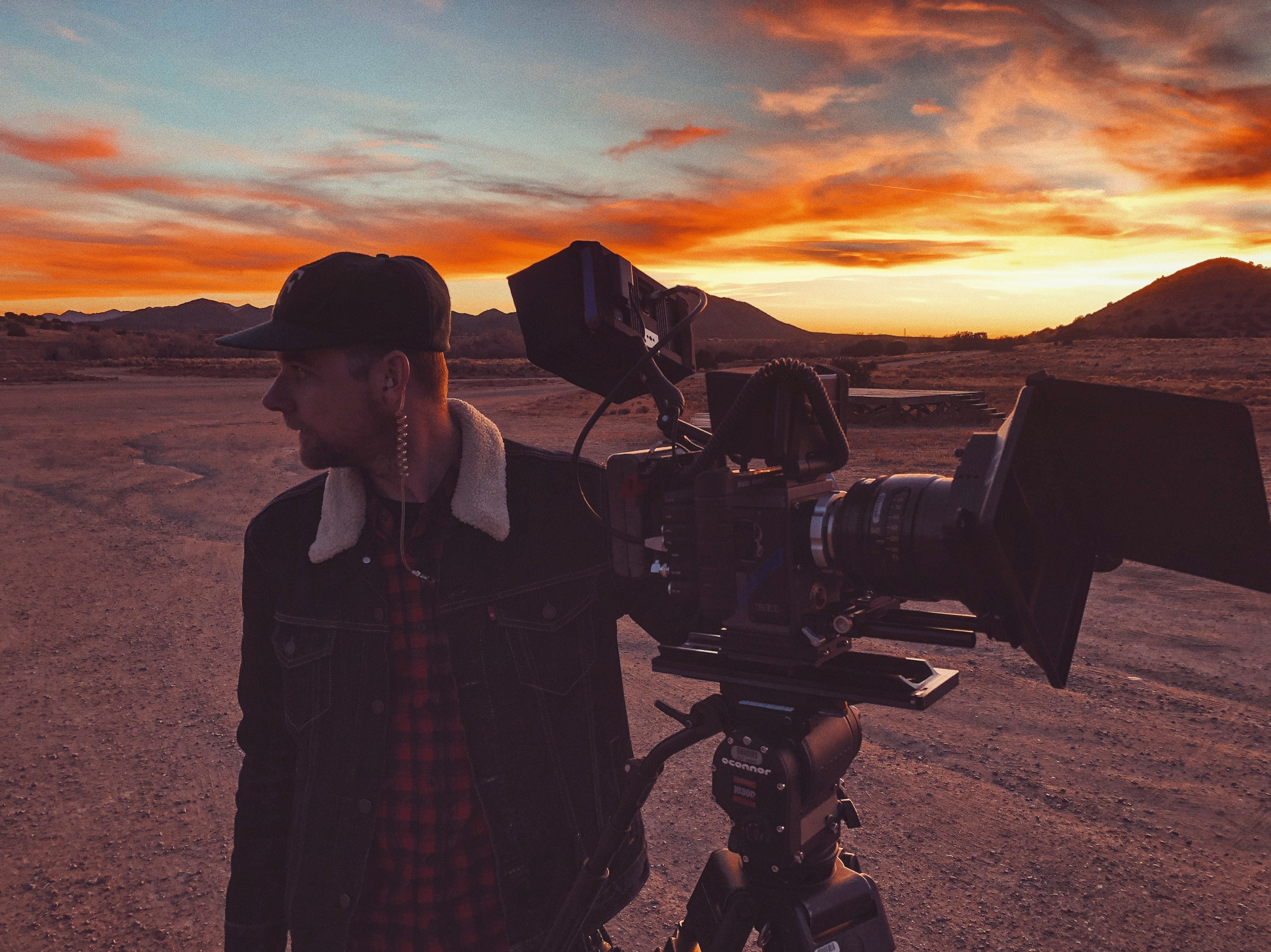 A man with a big professional camera setup in the dessert at sunset