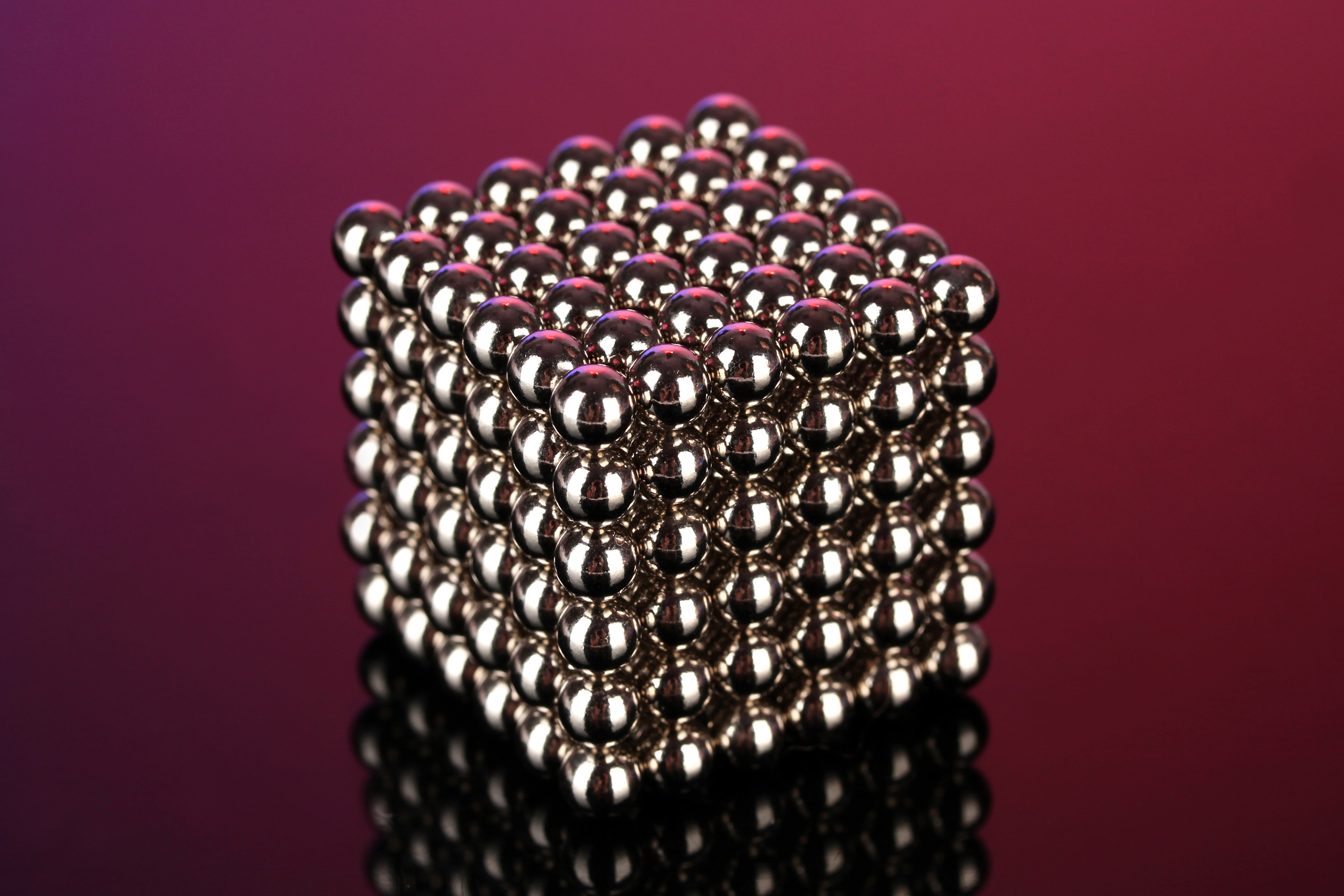 Metallic sphere cube structure on a glossy surface against a pink background.