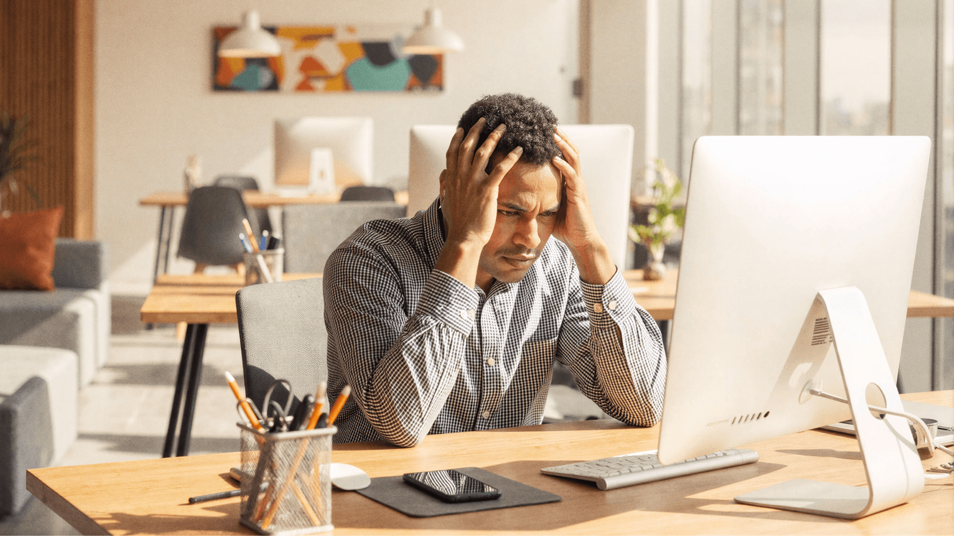 Profissional em ambiente de escritório, sentado diante de um computador, com as mãos na cabeça e expressão de preocupação, representando dificuldades na cobrança e gestão financeira em clínicas que buscam mais controle com a Tivita.