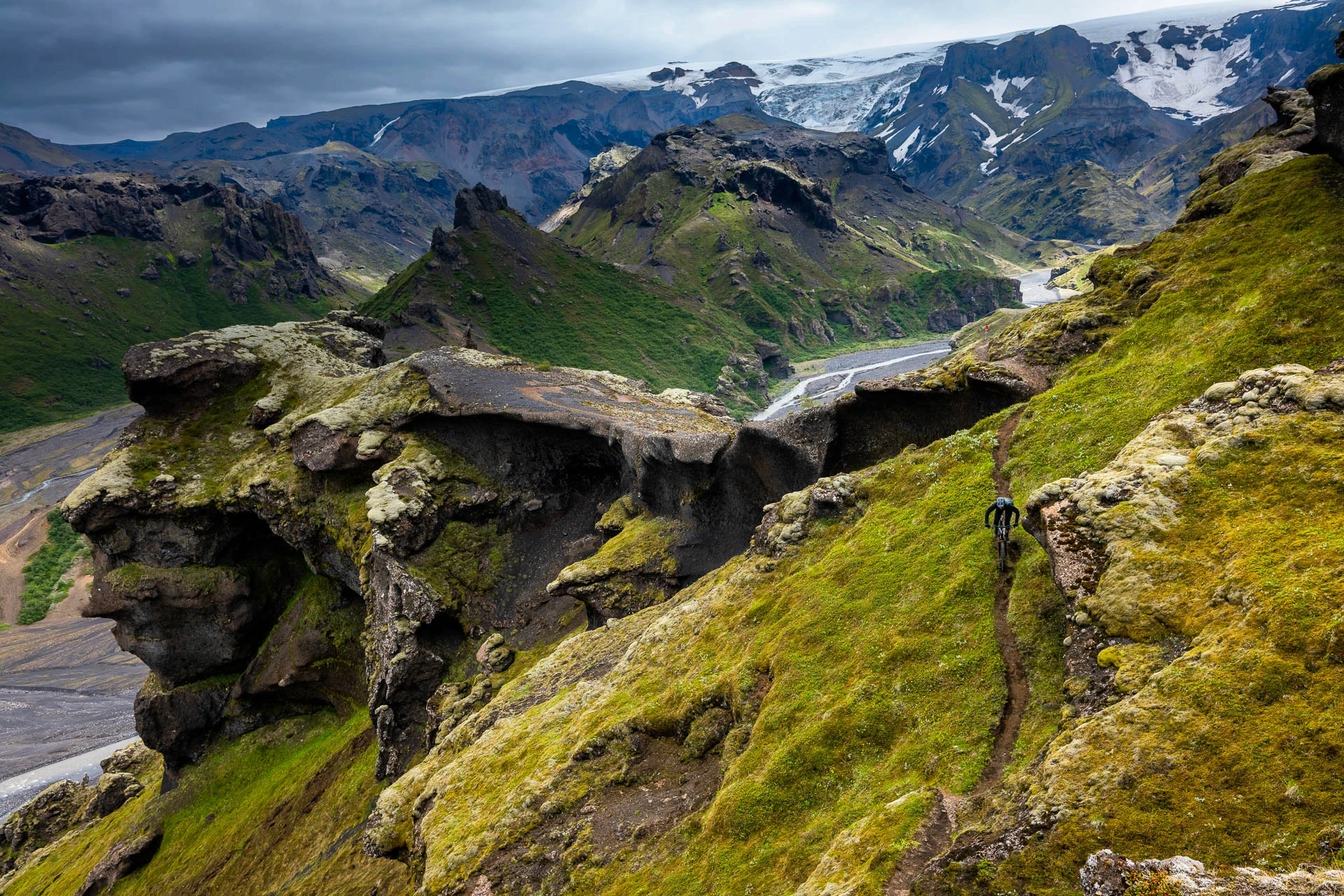 Mountain biker on a narrow trail above a green canyon and winding river.