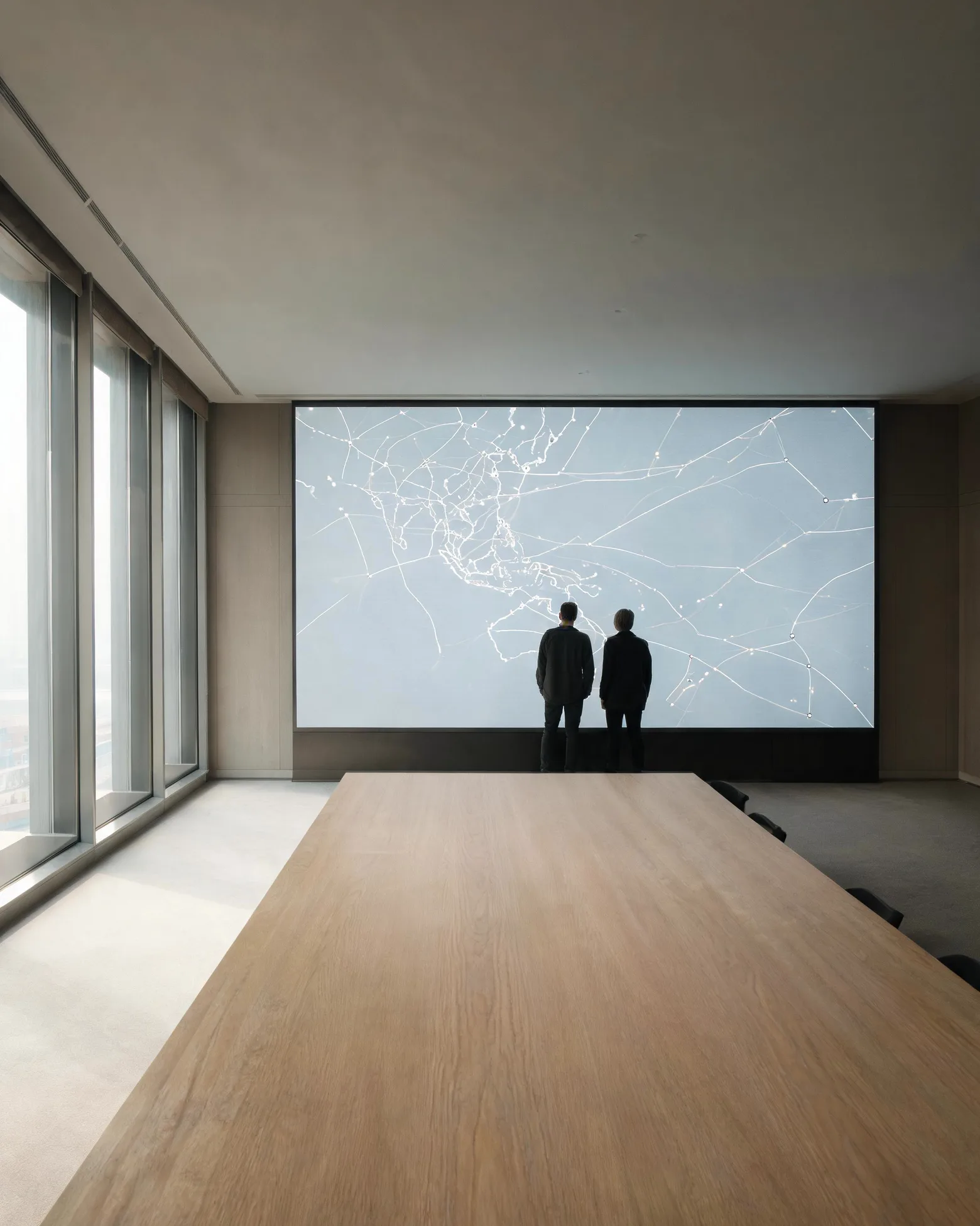 A planning room with a long table and two planners studying a wall-sized network map of shipping lanes