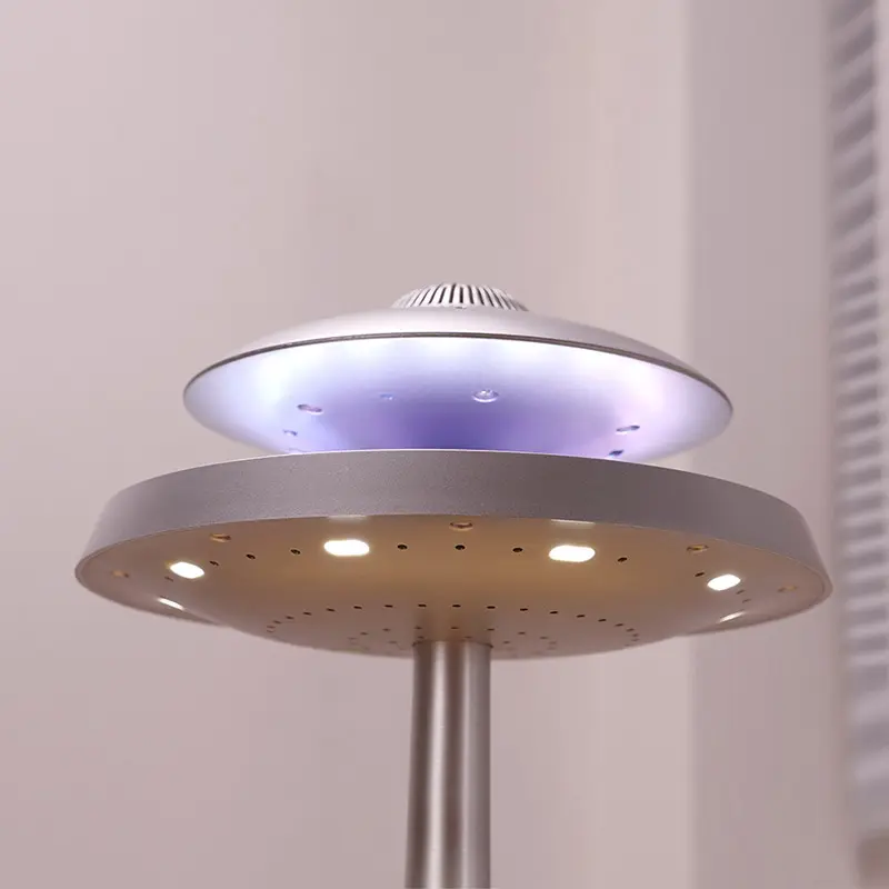 A lamp resembling a UFO design with a metallic base and a circular, disc-like top emits soft, multicolored lights. The background features a window with blinds.