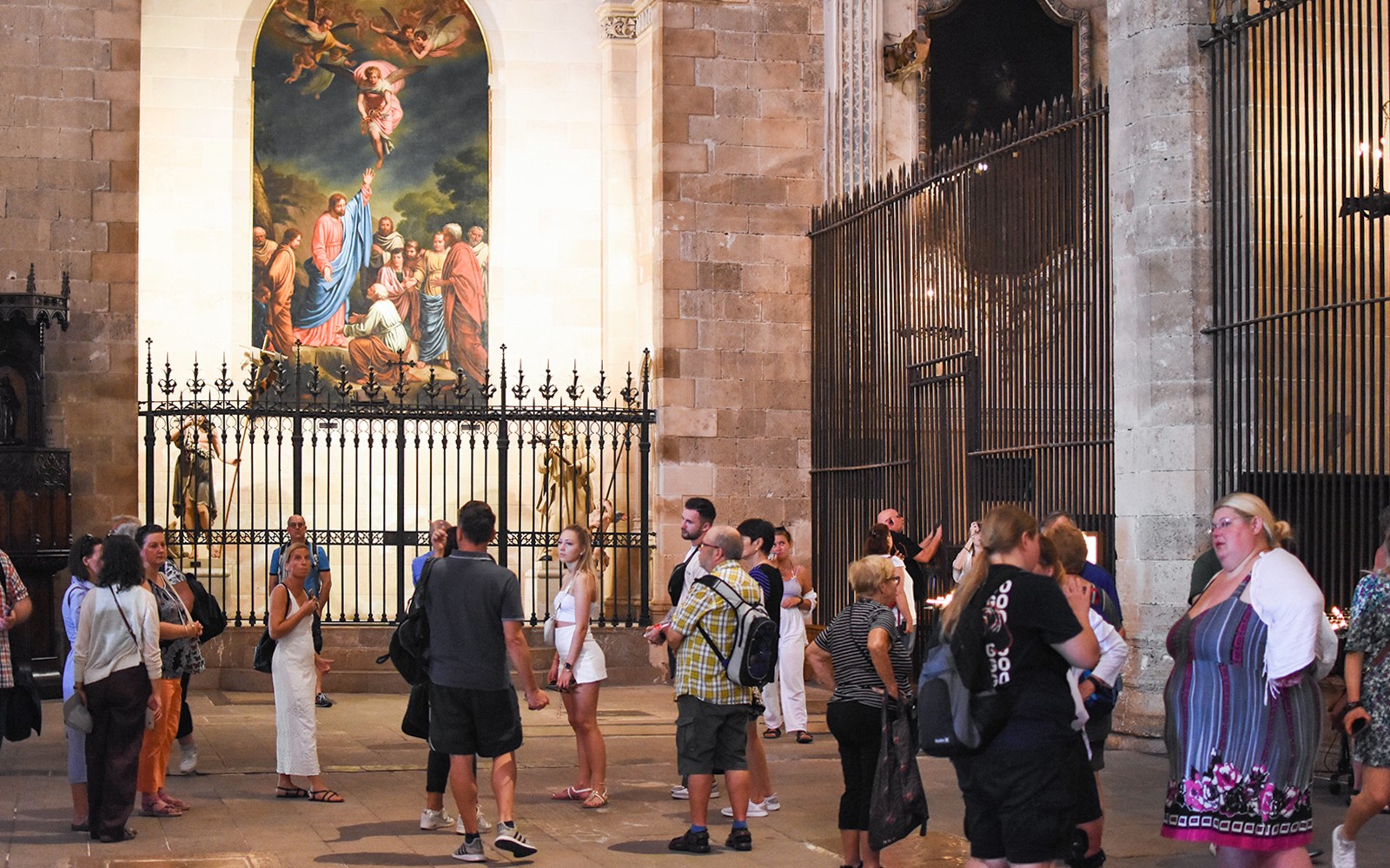 Turistas explorando el interior de la Catedral de Palma, en Mallorca, con una pintura religiosa al fondo.