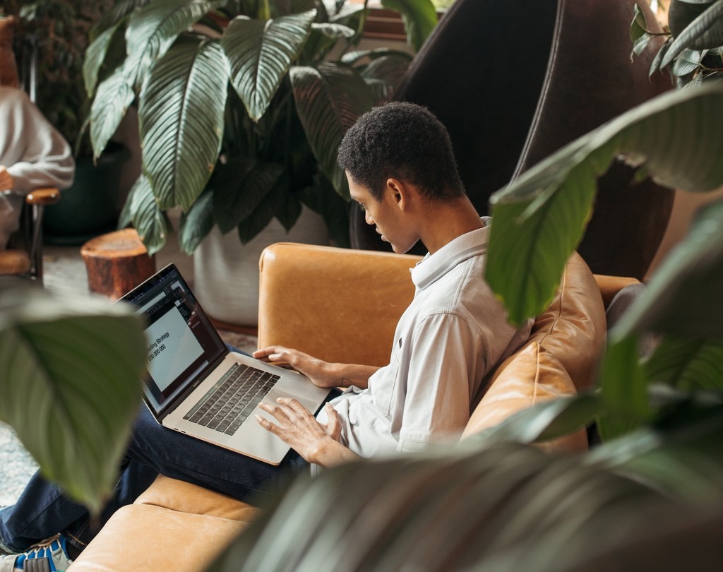 Man working on a laptop in a cozy plant-filled space.