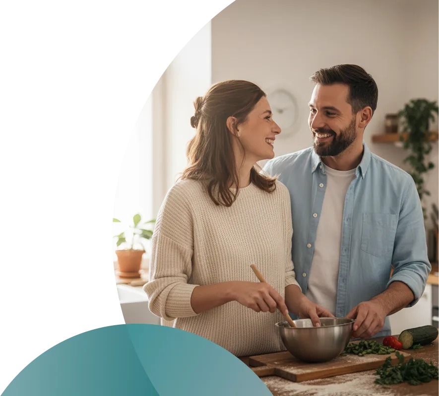 Couple cooking together in a bright kitchen while smiling at each other.