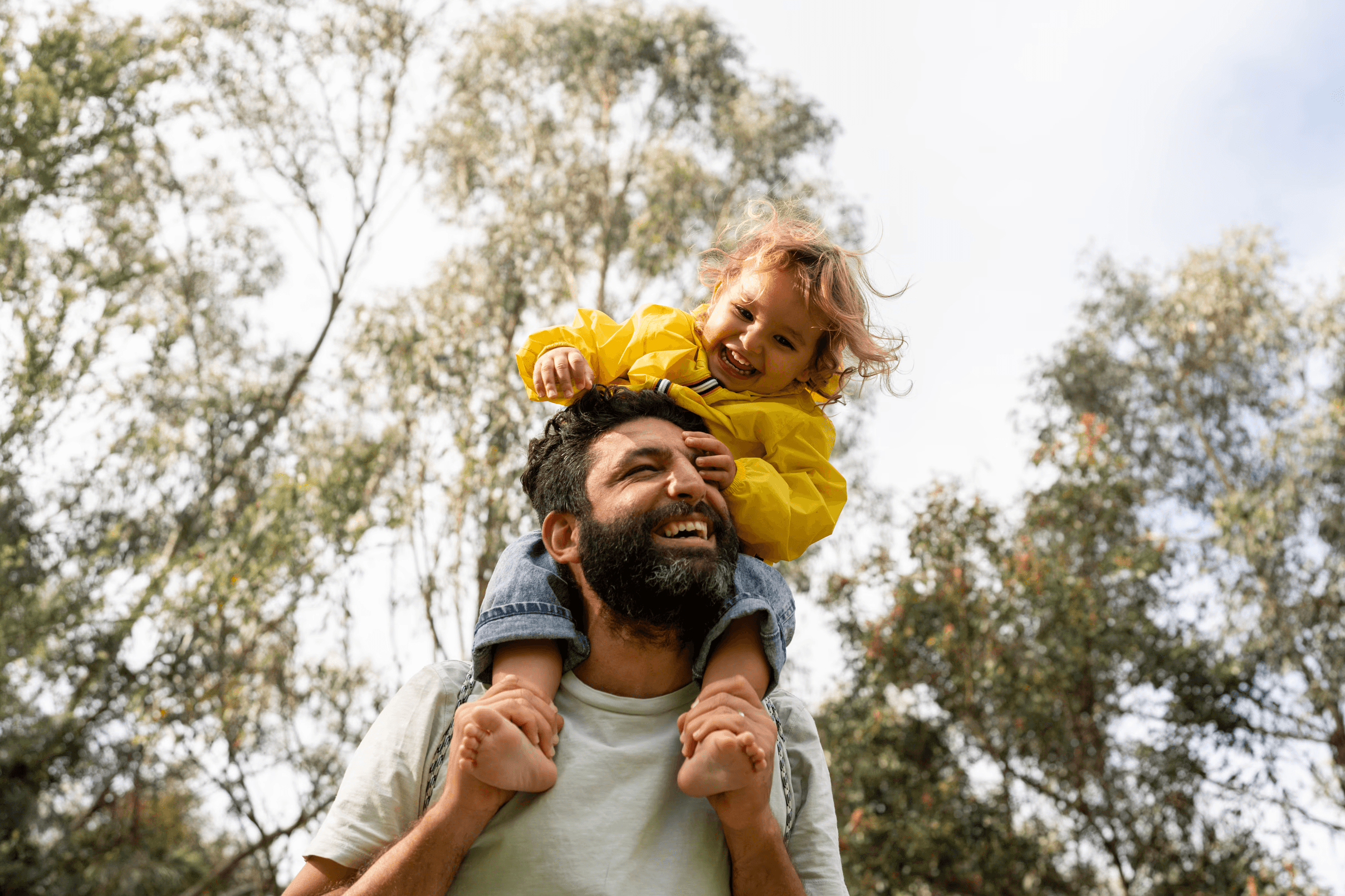 A dad with his daughter on his shoulders under trees