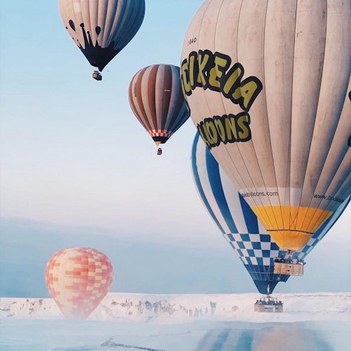 Iba't ibang kulay at disenyo ng mga hot air balloon na lumulutang sa asul na kalangitan sa itaas ng niyebeng tanawin.