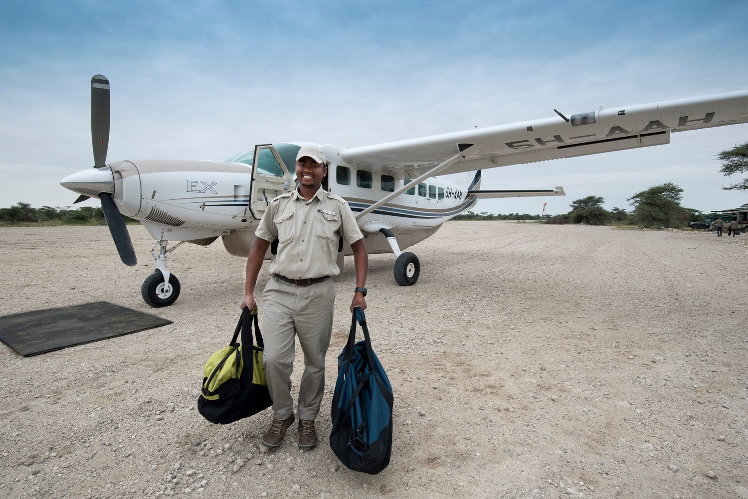 A bush plane on a Serengeti airstrip, camp staff carrying soft duffel bags