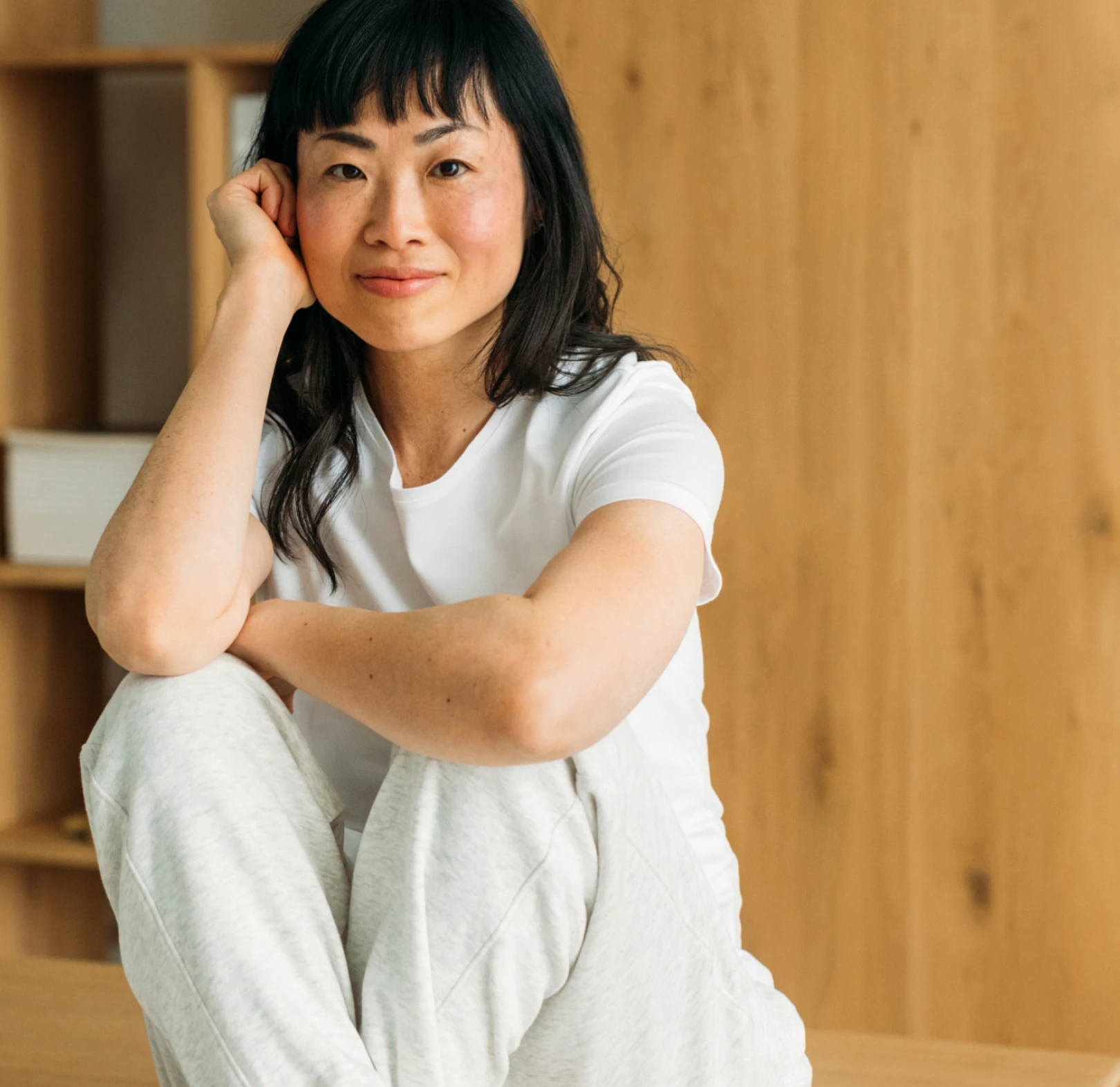A woman named Jenny O with black hair smiles while sitting on a wooden surface, with shelves in the background.