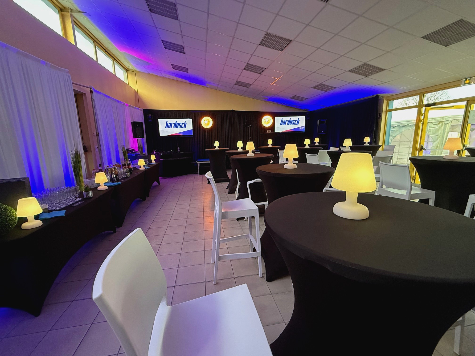 Modern indoor space with large glass doors, lush greenery, and a cozy seating area visible beyond.