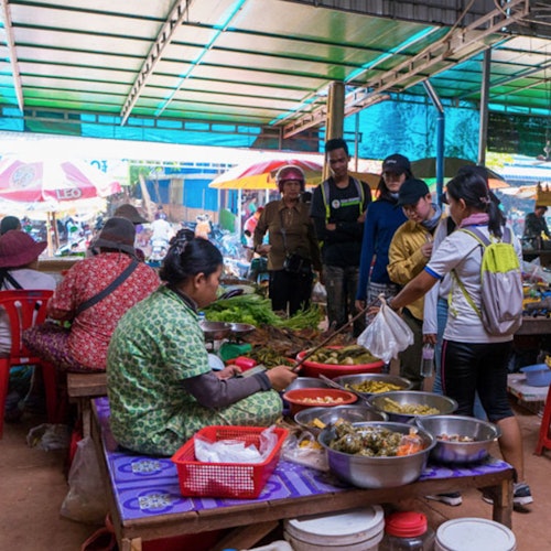 人们在一个热闹的市场摊位上交流，在金属顶棚下有各种食品和商品。