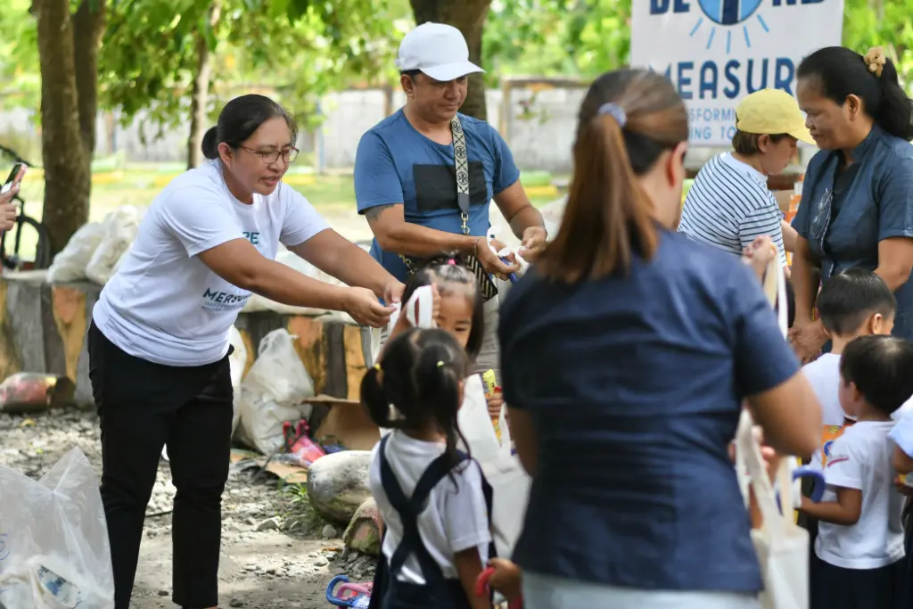 Volunteers handing out school supplies to students under the trees