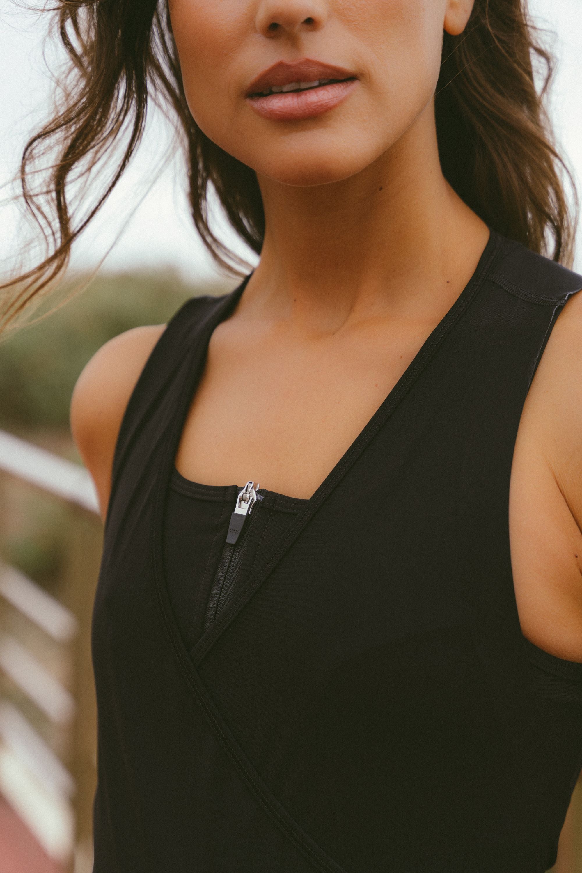 Extreme-close-up-shot-focusing-on- the-neckline-of-a-black-athletic- cycling-garment-showing-the-detail- of-a-silver-zipper-pull-at-the-center- of-the-chest-The-garment-features-a-V-neck-overlapping-design-over-a-high-neck-inner-layer-The-model's-chin-and-mouth-are- partially-visible-in-the-top-of-the- frame