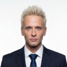 Portrait of a woman with long, smooth hair swept to the side, in a dark t-shirt, on a plain background.