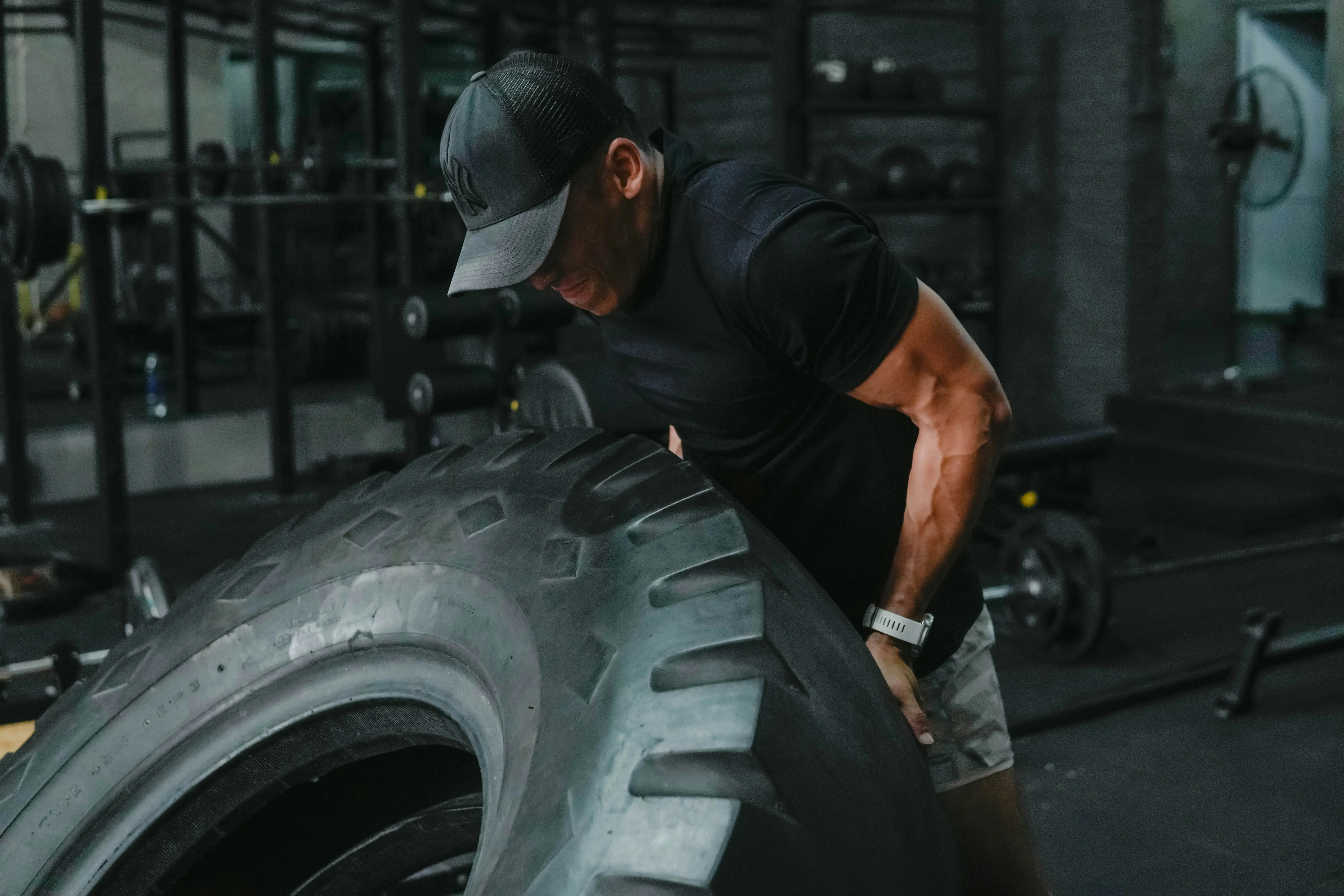 Strong man lifting and flipping a large tractor tire during an intense strength workout in the gym.
