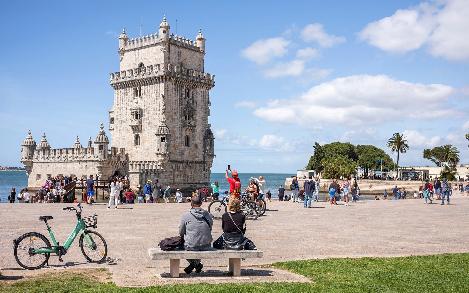 在电动嘟嘟车半日游中,可以看到里斯本的贝伦塔,周围有游客和骑自行车的人。