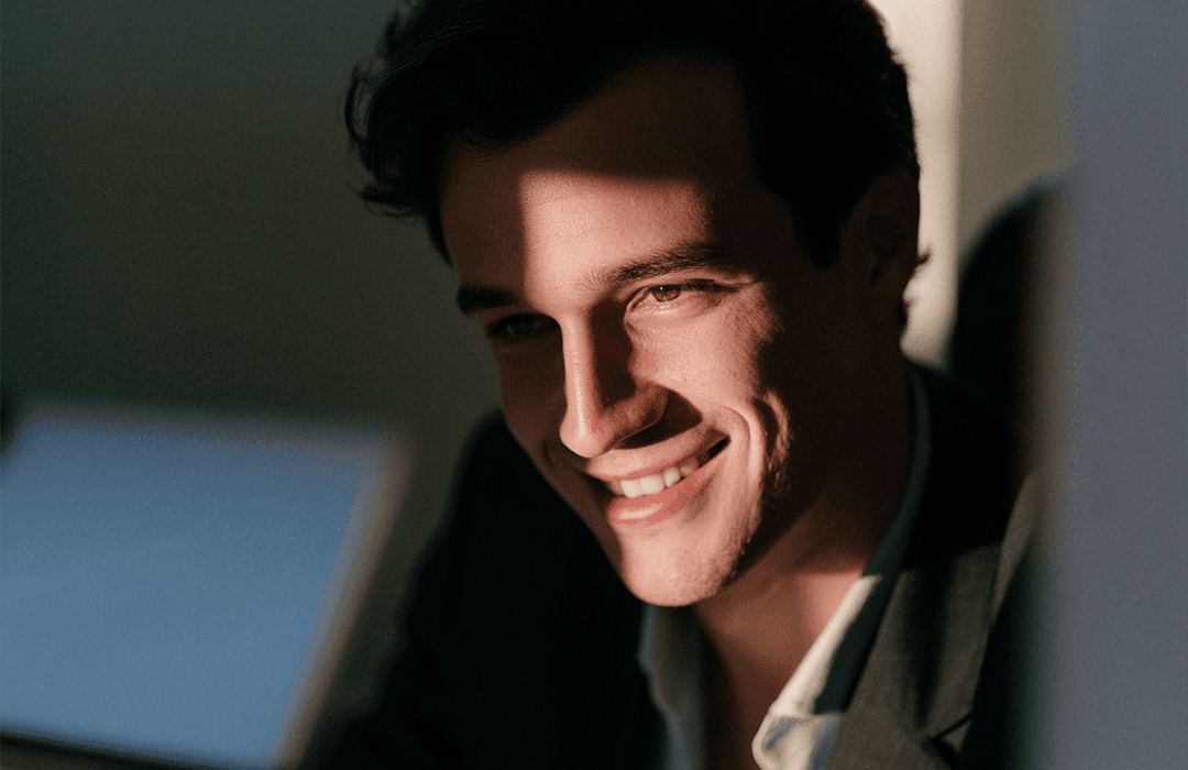 Homem sorrindo com iluminação de sombras no rosto em ambiente corporativo.
