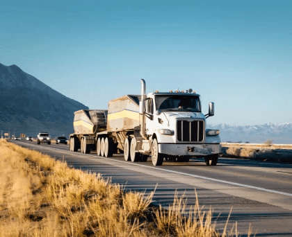 White semi-truck with trailer driving on a mountain highway during daylight.