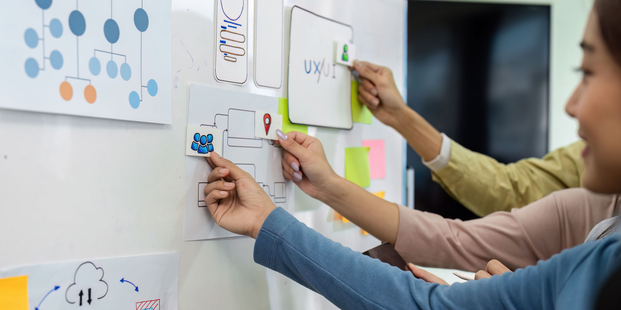 Specjaliści z agencji reklamowej planują architekturę informacji oraz interfejs użytkownika na białej tablicy podczas sesji projektowej.