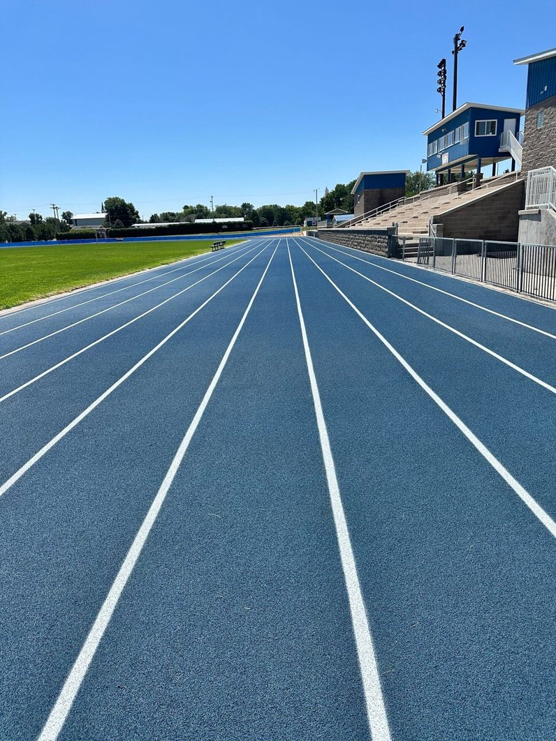 Blue outdoor running track with clearly marked lanes, showing a well-maintained surface used as an example of proper running track maintenance.