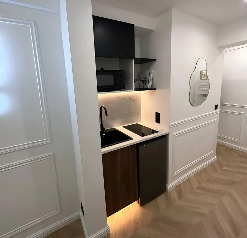 Cuisine compacte et design avec placards noirs et bois, plan de travail sombre et miroir rond à l'entrée.