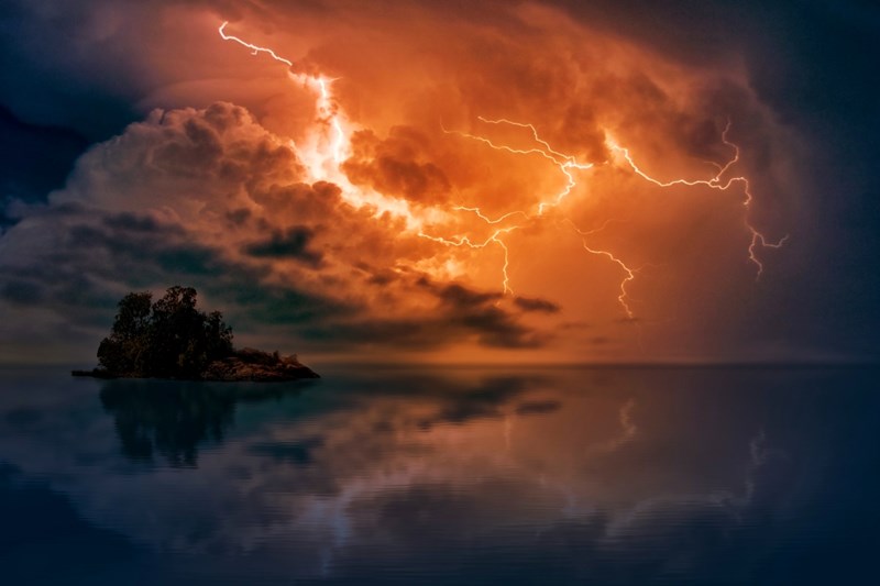 Lightning striking above a small island in the ocean reflected in dark dramatic water