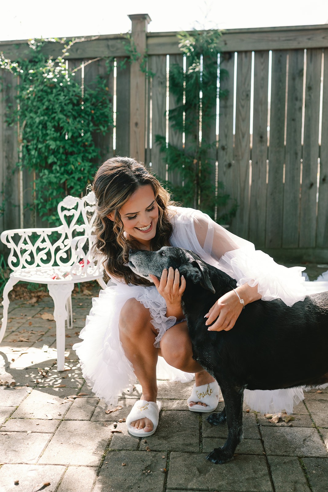 Bride laughing as the groom holds their brown puppy close to her face.