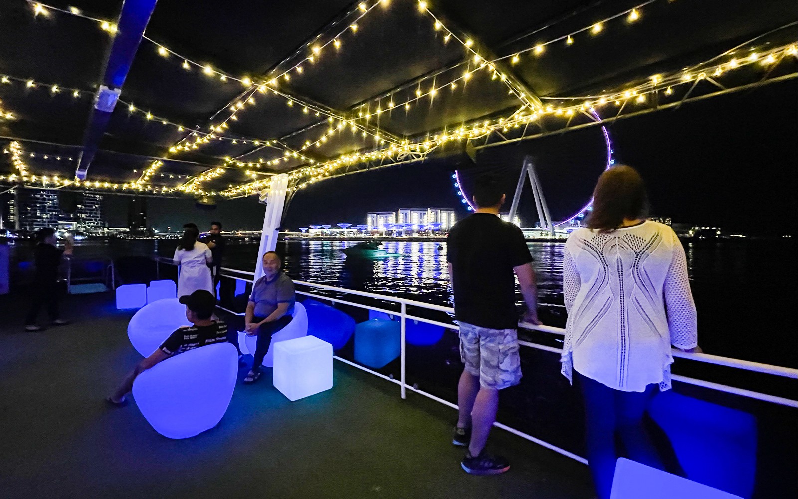 Hausboot-Deck mit Menschen, die den nächtlichen Blick auf das Riesenrad Ain Dubai genießen.
