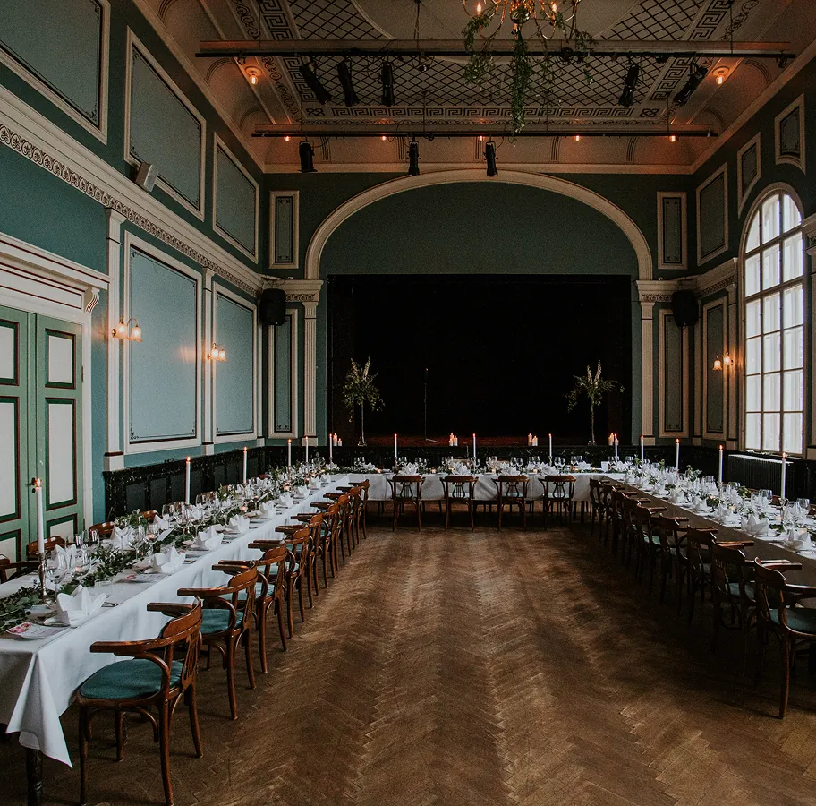 Банкетный зал с высокими потолками, арочными окнами и U-образной расстановкой столов с цветами