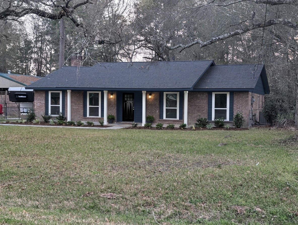 Brick house exterior update — ranch with navy trim, white columns, black door, foundation plantings