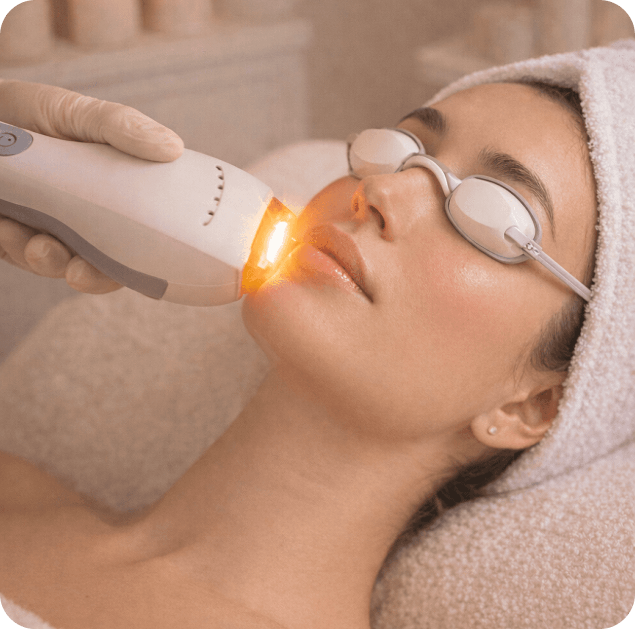 Woman in a towel applying pink under-eye gel patches while looking into a mirror on a vanity table