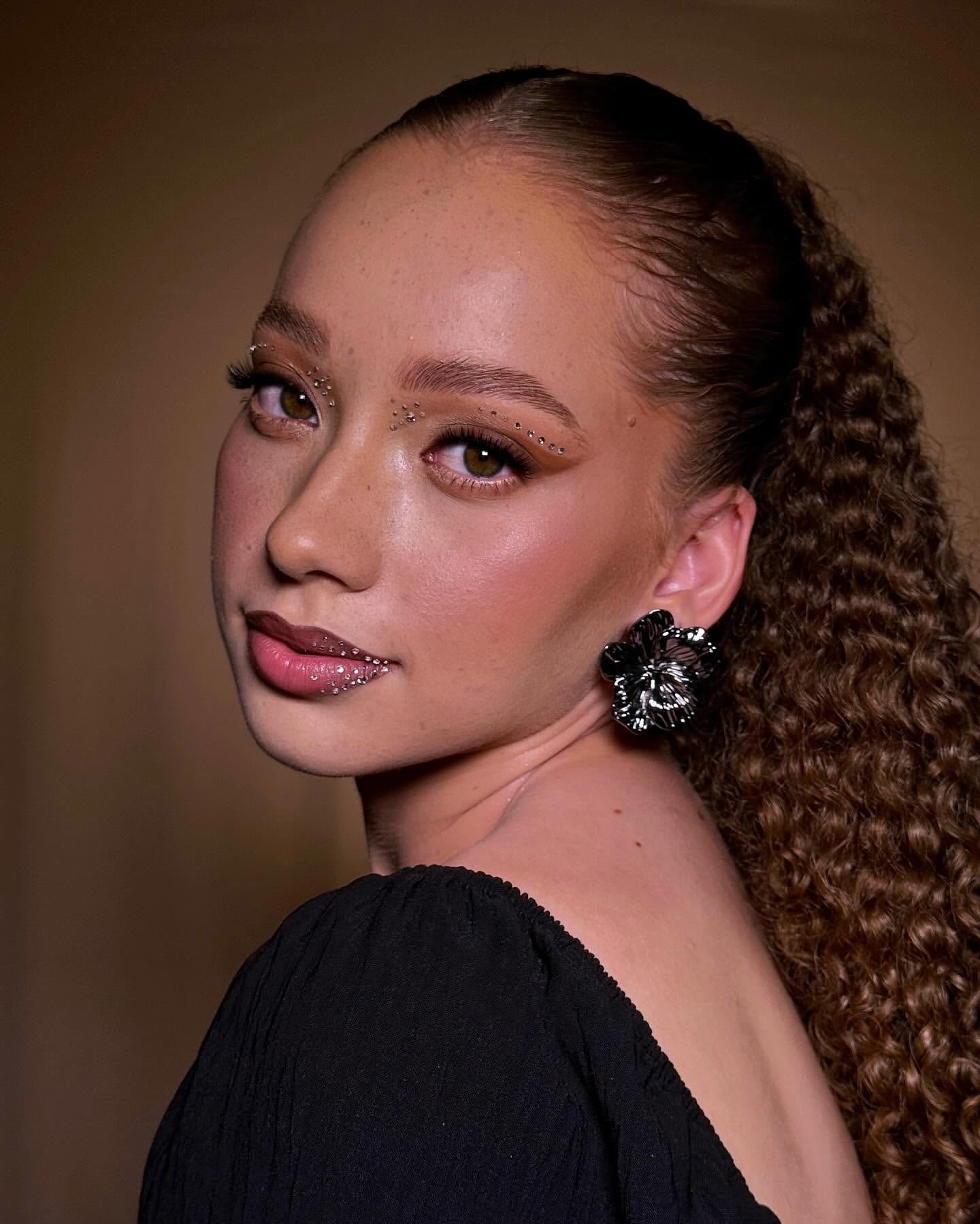 Cliente com maquiagem natural e delicada, assinada por Pry Sanches Beauty. A profissional de beleza realçou a pele com leveza, optando por um visual fresh com lábios rosados e cílios alongados. O cabelo cacheado com acessórios sofisticados dá um toque de modernidade, sendo perfeito para festas e eventos de alta classe. Maquiagem minimalista com foco na realce dos traços naturais.